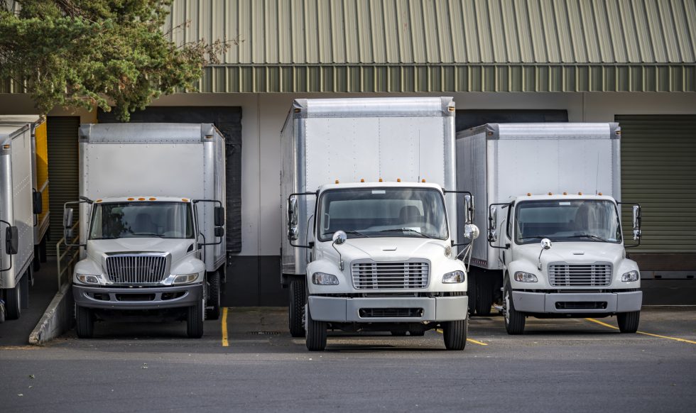 Useful Industrial standard for local deliveries and short haul freights compact middle duty rigs semi trucks with box trailers standing in warehouse dock with gates loading cargo for next delivery